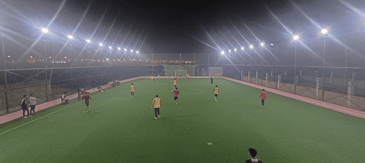 Friends playing football under floodlights on a netted Bangladesh turf